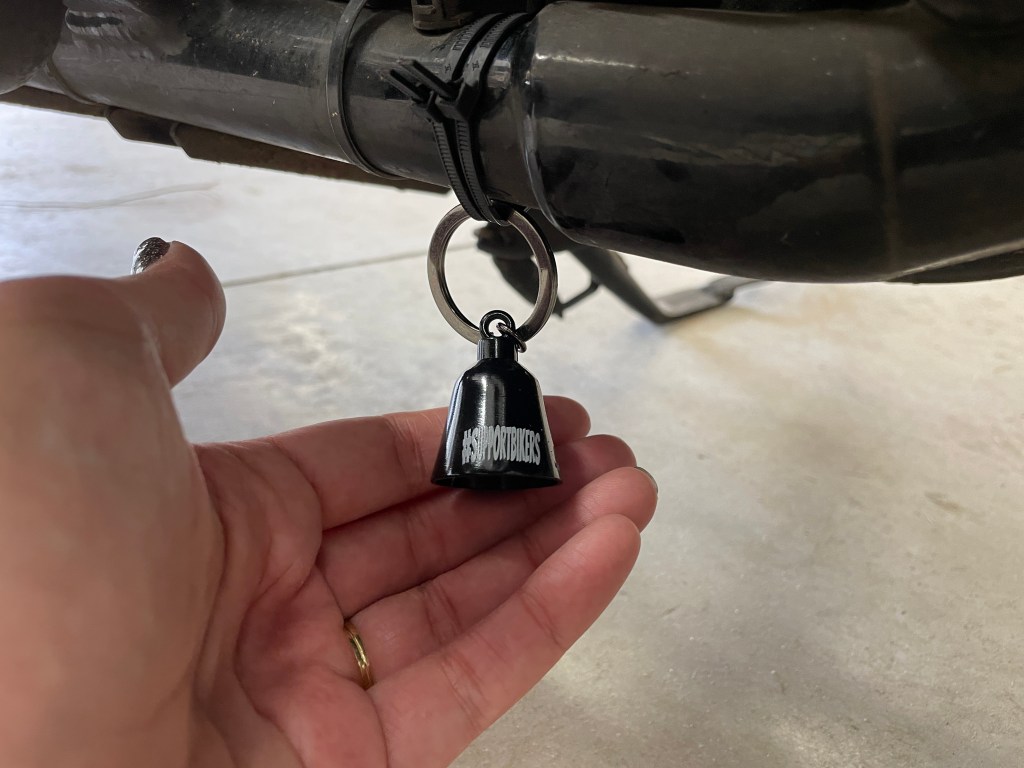hand holding bell hanging from the bottom of a motorcycle - gremlin bell tradition