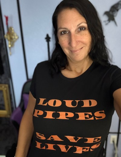 lady wearing a black shirt with orange writing that says loud pipes saves lives