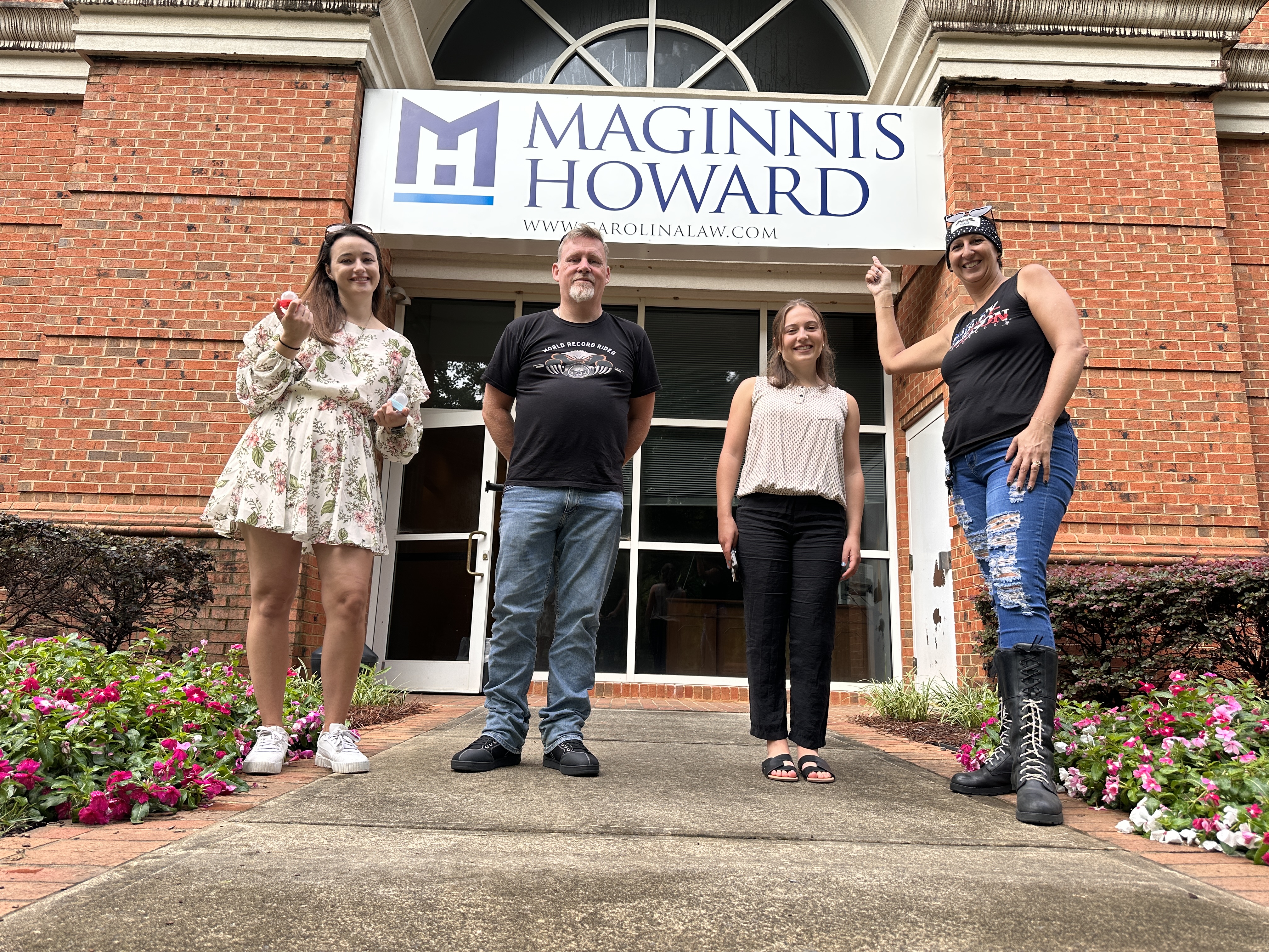 4 individuals standing and pointing at the Maginnis Howard Law Firm Sign